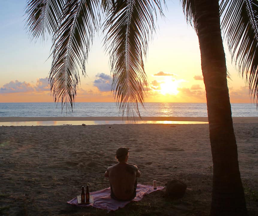 Man sitting under a palm tree at a beach Mexico Pacific coast