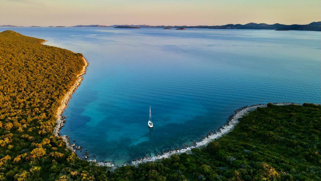 An aerial photo of boat anchored by itself in a small cove at sunset.