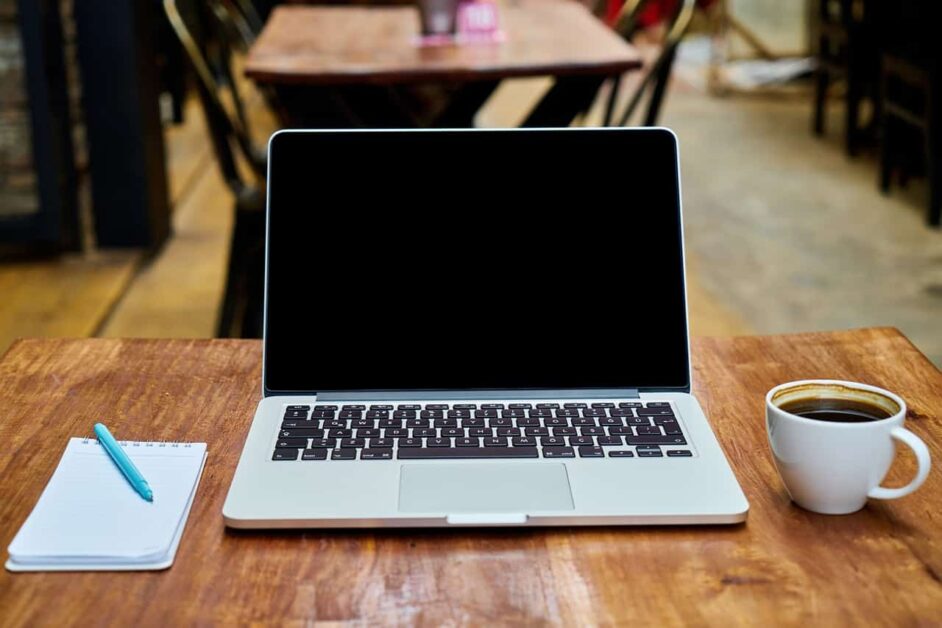 A laptop open next to a notebook and a cup of coffee in a cafe