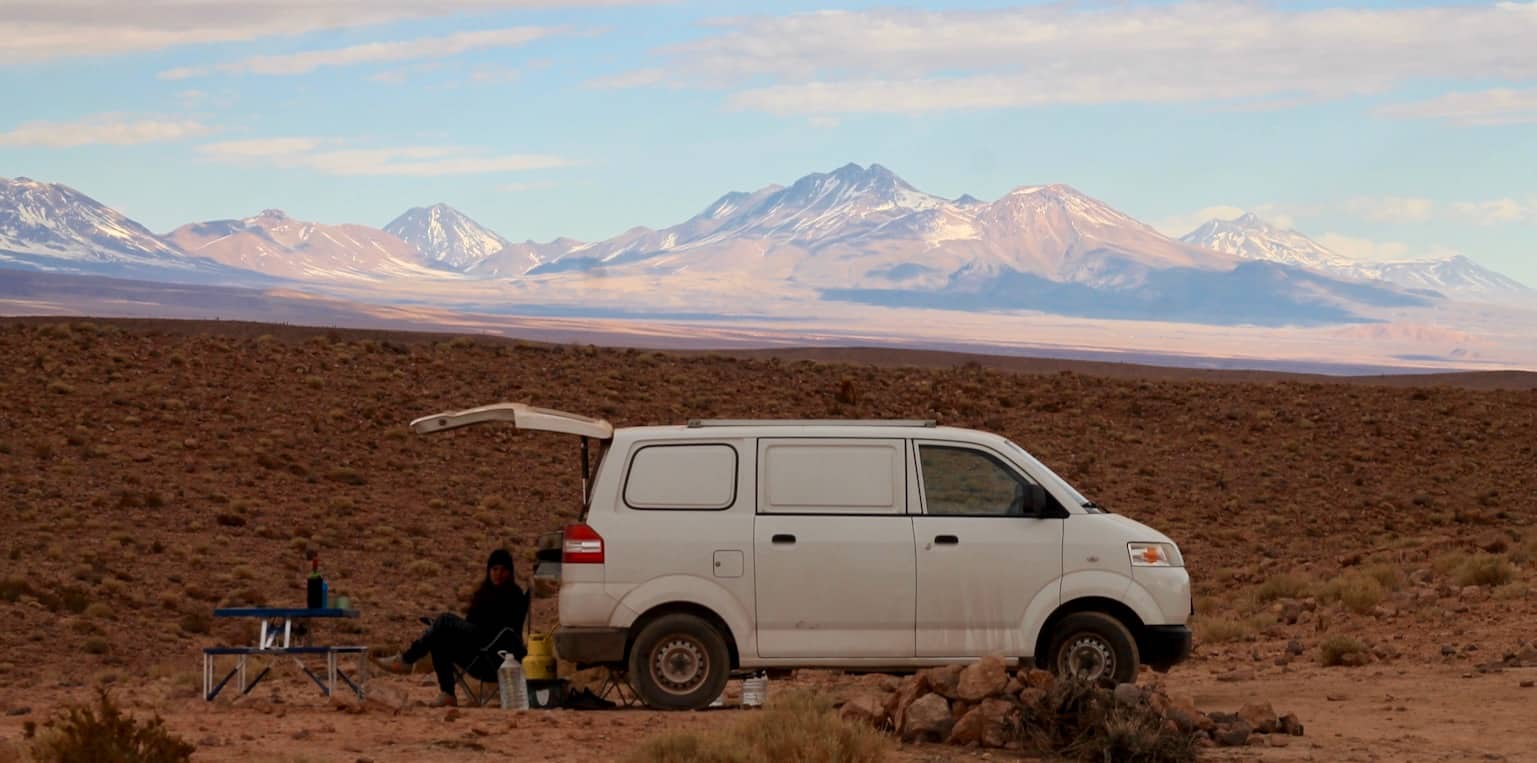 A woman camped in the desert, snow-capped mountains in the distance